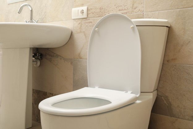 Close-up of a modern ceramic toilet bowl beside a sink in a beige tiled bathroom, design inspiration from Sims Lighting Gallery for toilet bowl Singapore